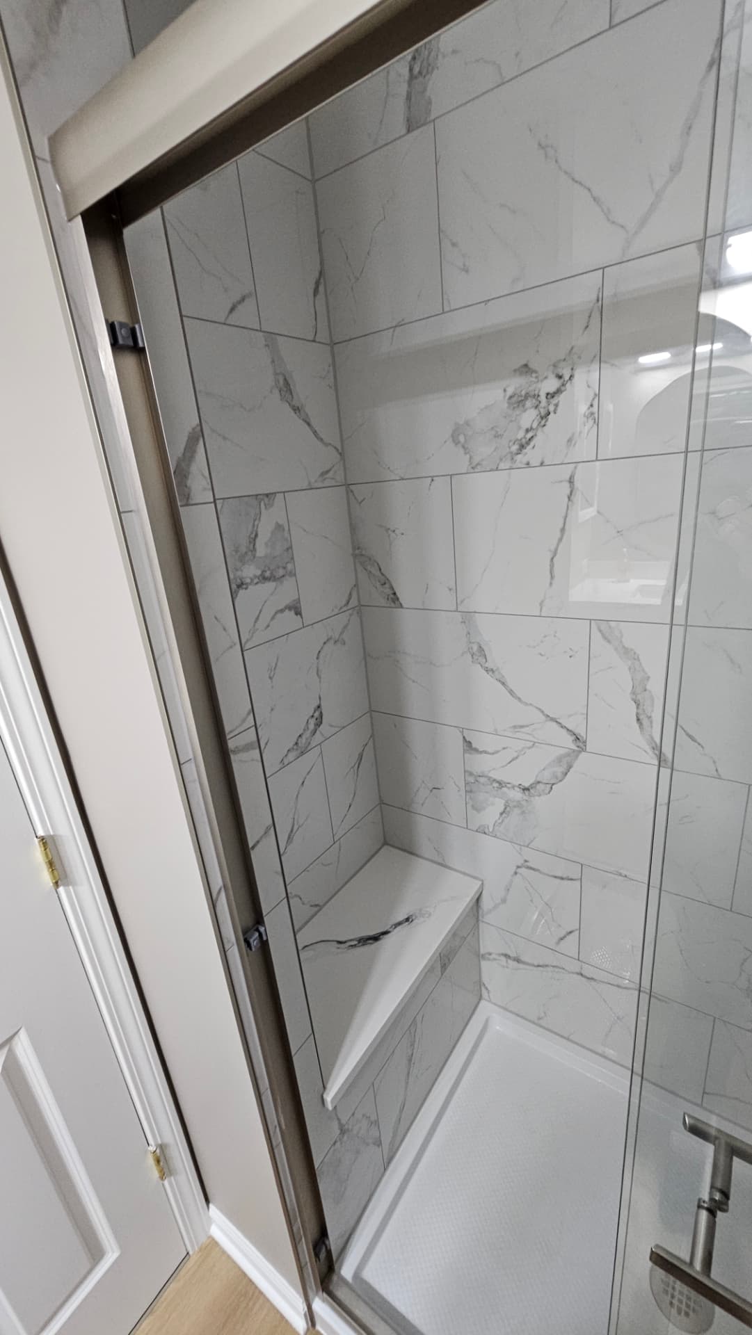 Marble-look tiled shower with a corner bench and aligned grout lines