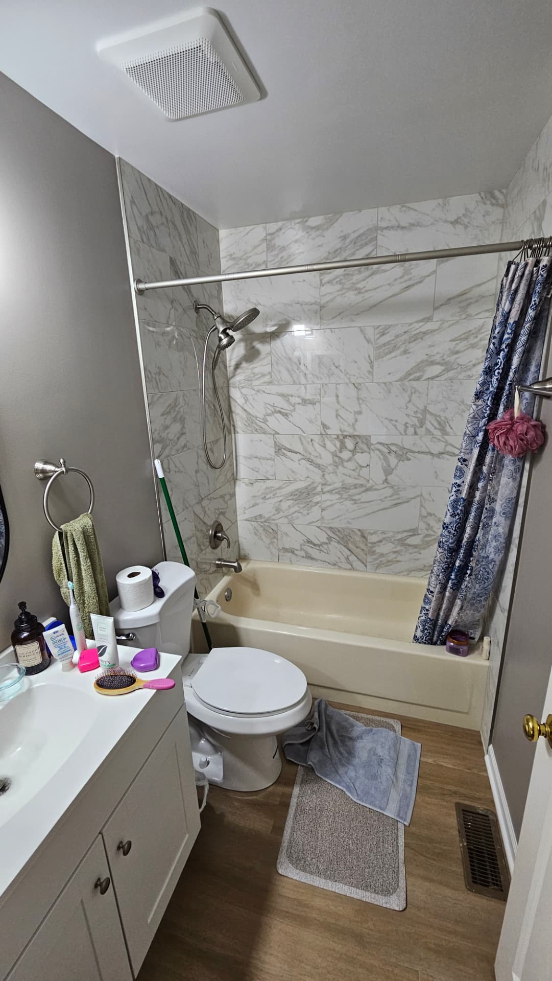 Bathroom with a newly tiled marble-look tub surround, plank flooring and grey walls
