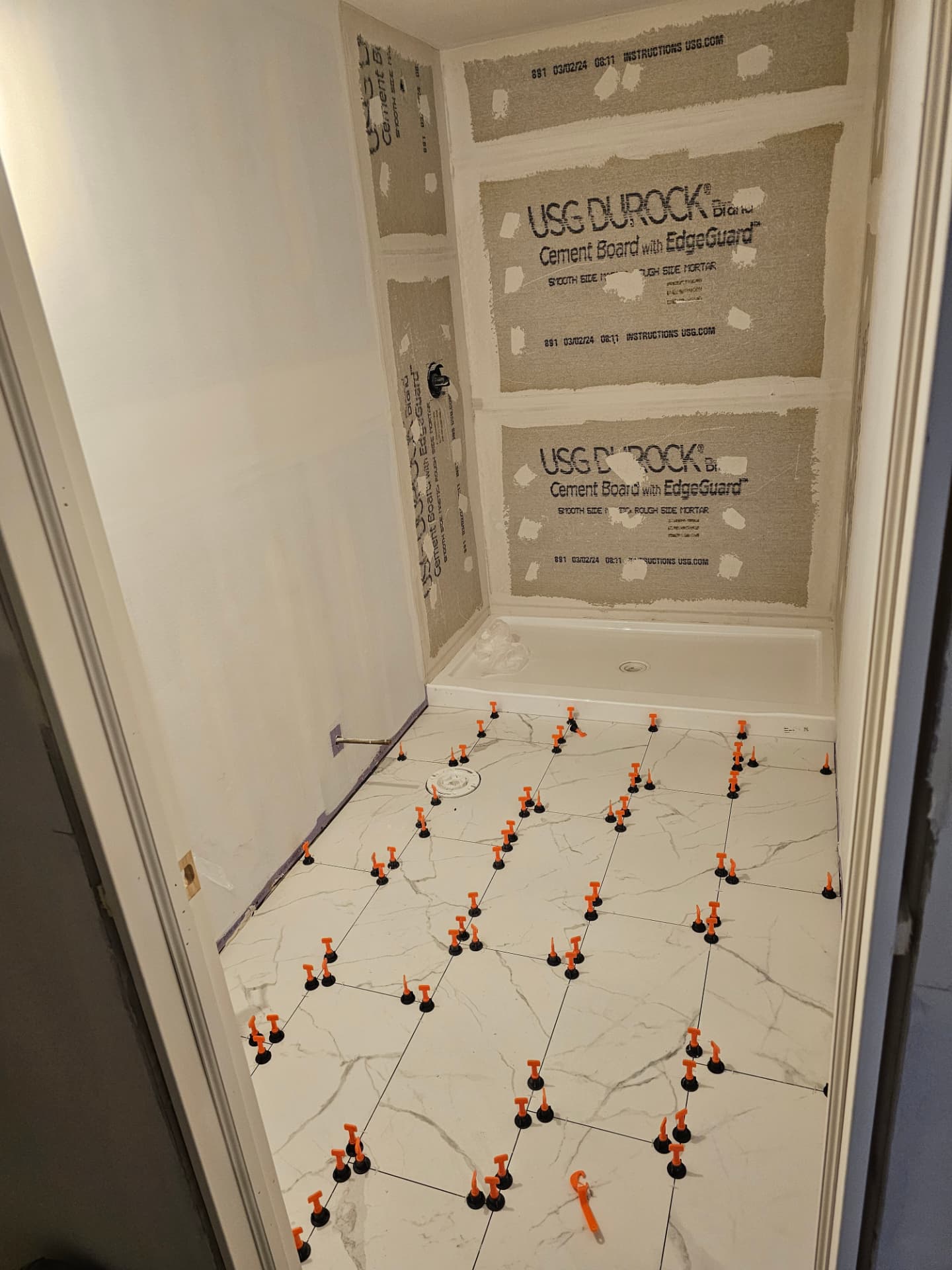 Bathroom in progress with cement board shower walls and floor tile set with leveling clips