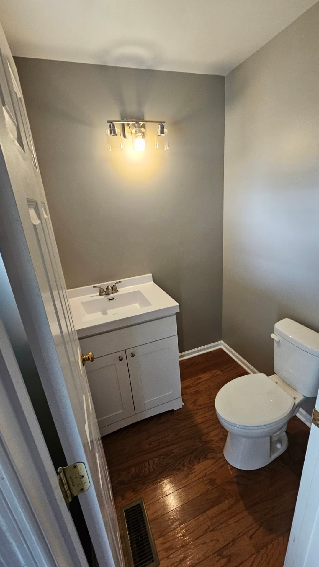 Refreshed powder room with grey walls, new white vanity, glass light fixture and hardwood floor