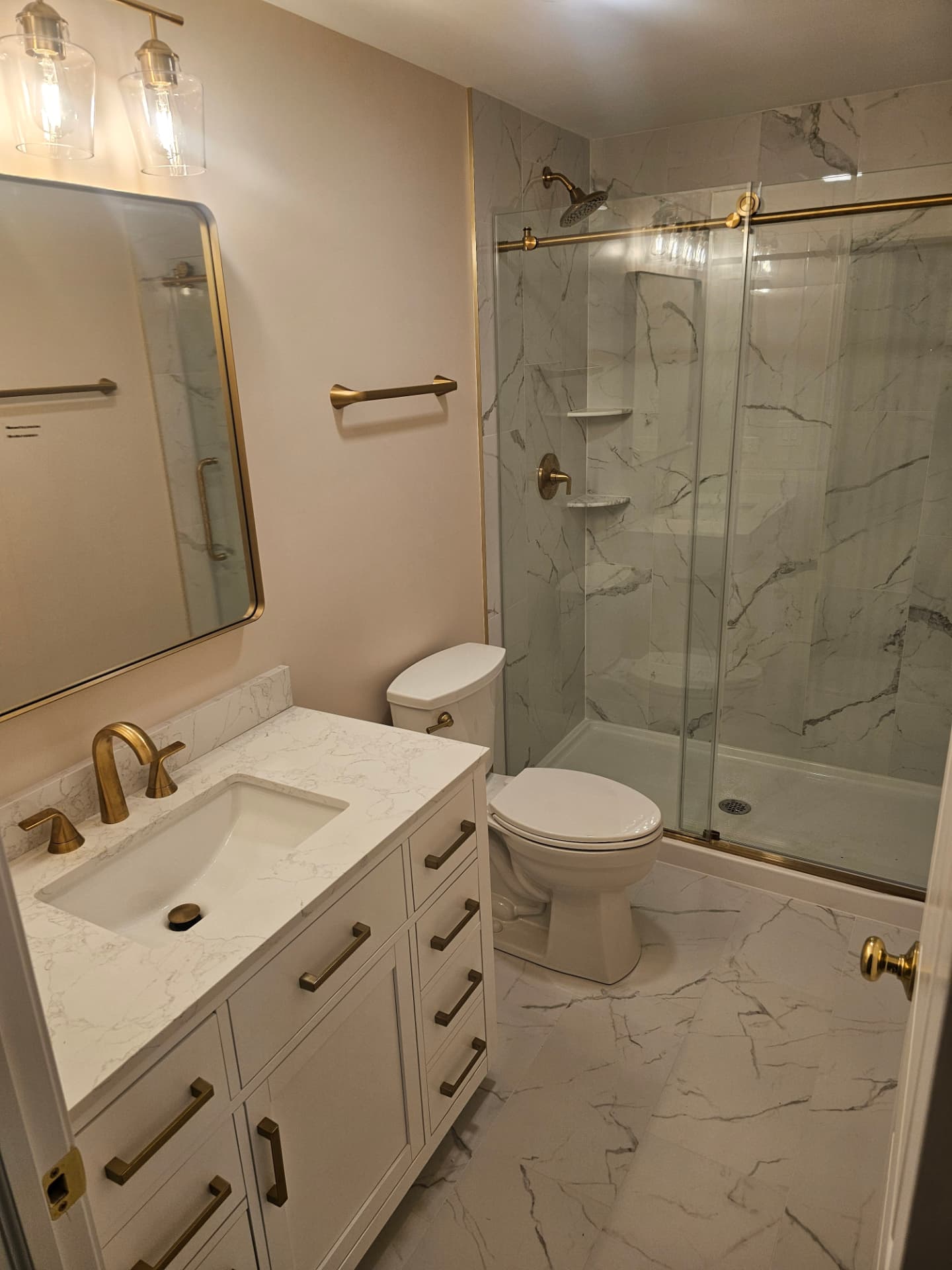 Second view of the finished bathroom showing the vanity, brass mirror and tiled shower