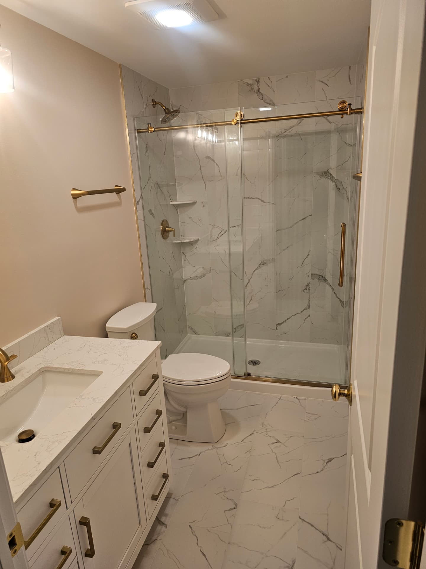Finished bathroom with marble-look tile shower, glass sliding door, brass fixtures and a white vanity