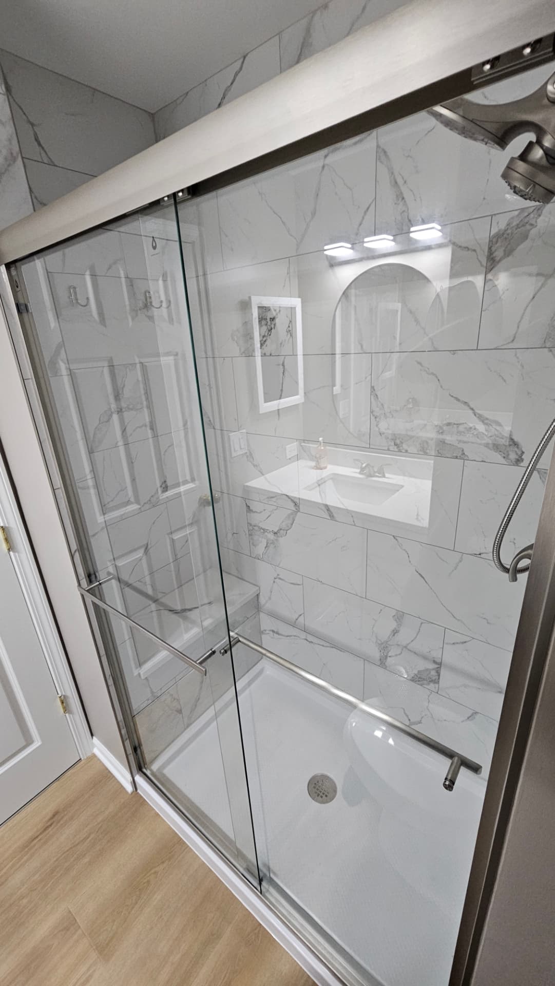 Walk-in shower tiled in white marble-look tile with a corner bench and sliding glass door