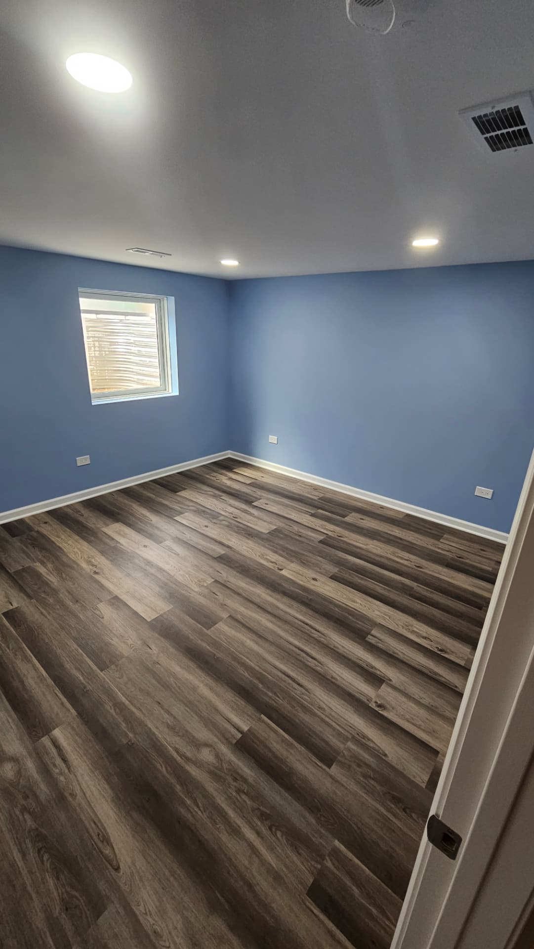 Finished basement bedroom with blue walls, white trim and grey-brown plank flooring
